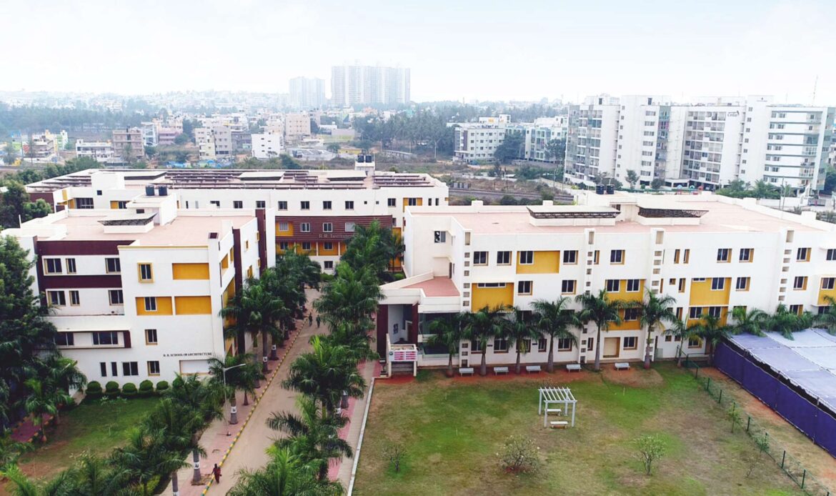 An elevated aerial view of the modern RR Institutions campus in Bangalore, featuring multi-story academic buildings with distinctive yellow and brown accents, palm trees, and a spacious green lawn, a premier hub for technical and medical education.